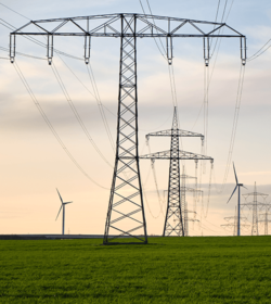 Long distance view on several transmission towers as part of a massive electrical power line on a green field, wind turbines in the background (C) Shutterstock, Gerrit Ebneter